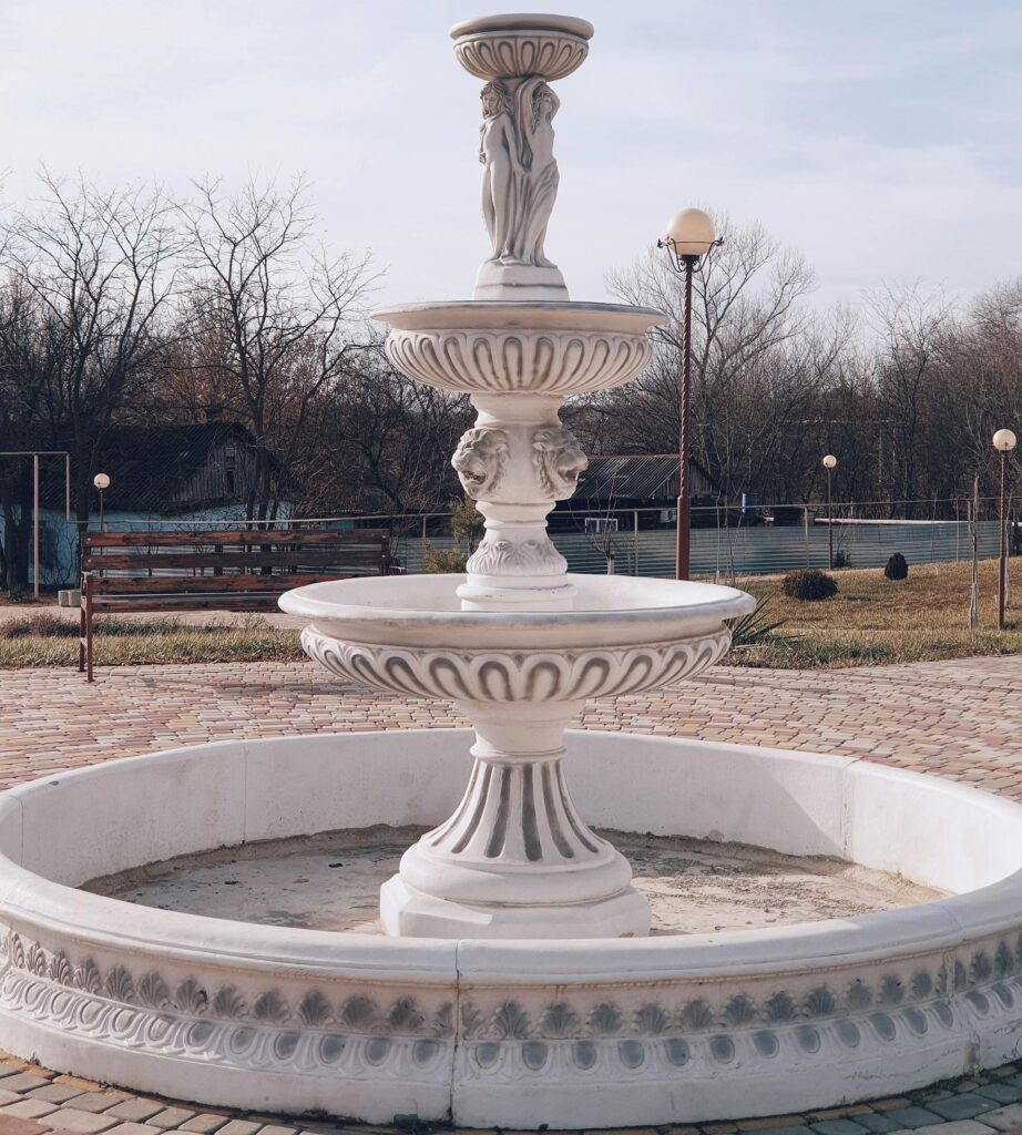 A beautifully ornate white marble water fountain in an outdoor setting, ideal for decorative garden themes.