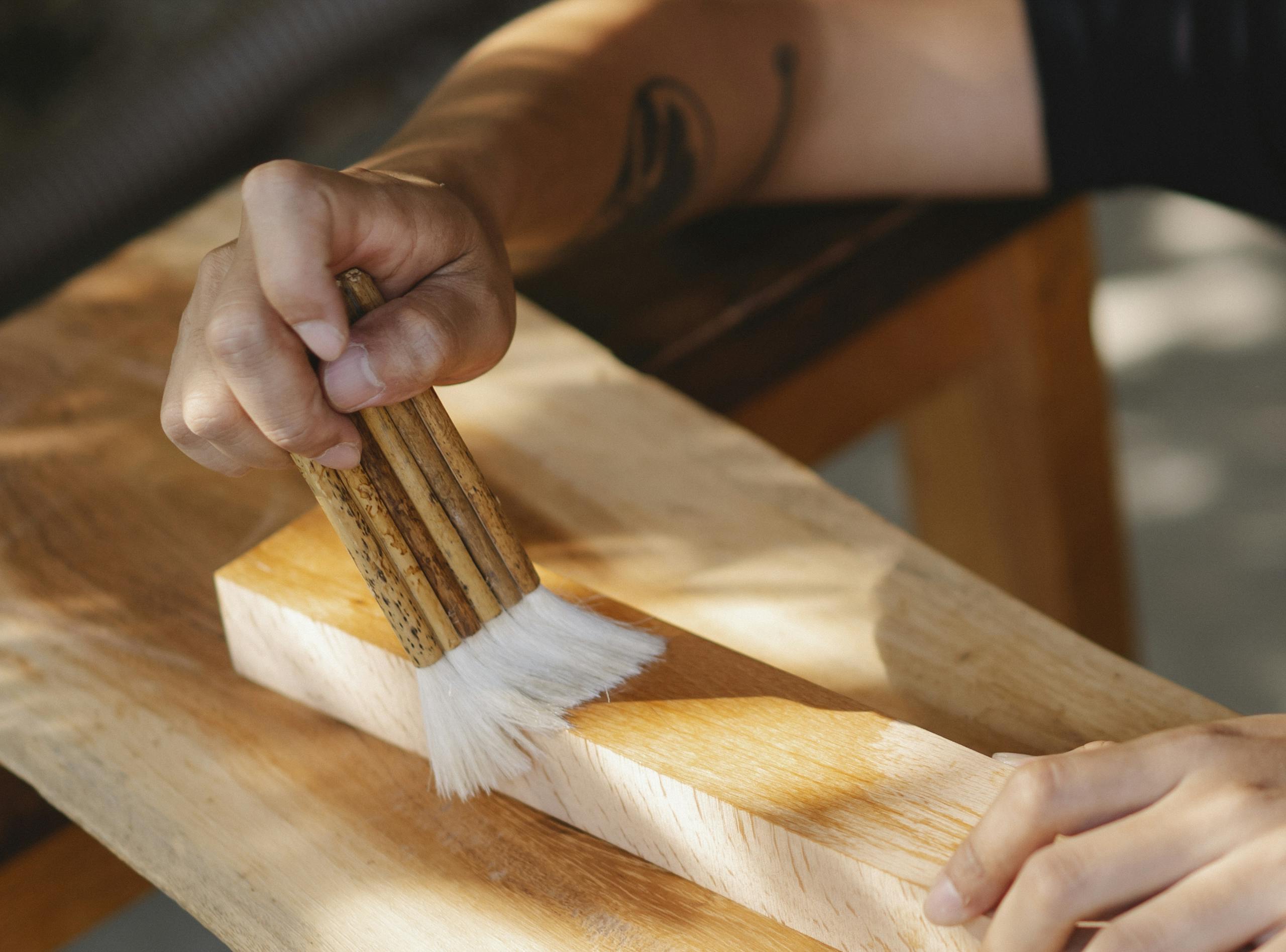 Close-up of an artisan applying varnish to wood with a brush.